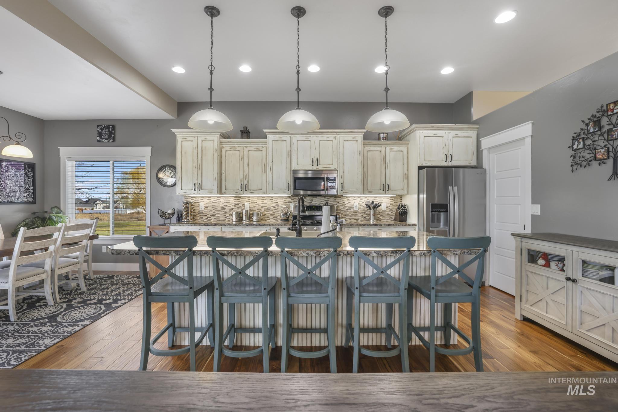 Kitchen with dark wood finished floors, decorative light fixtures, a kitchen breakfast bar, a center island with sink, and appliances with stainless steel finishes