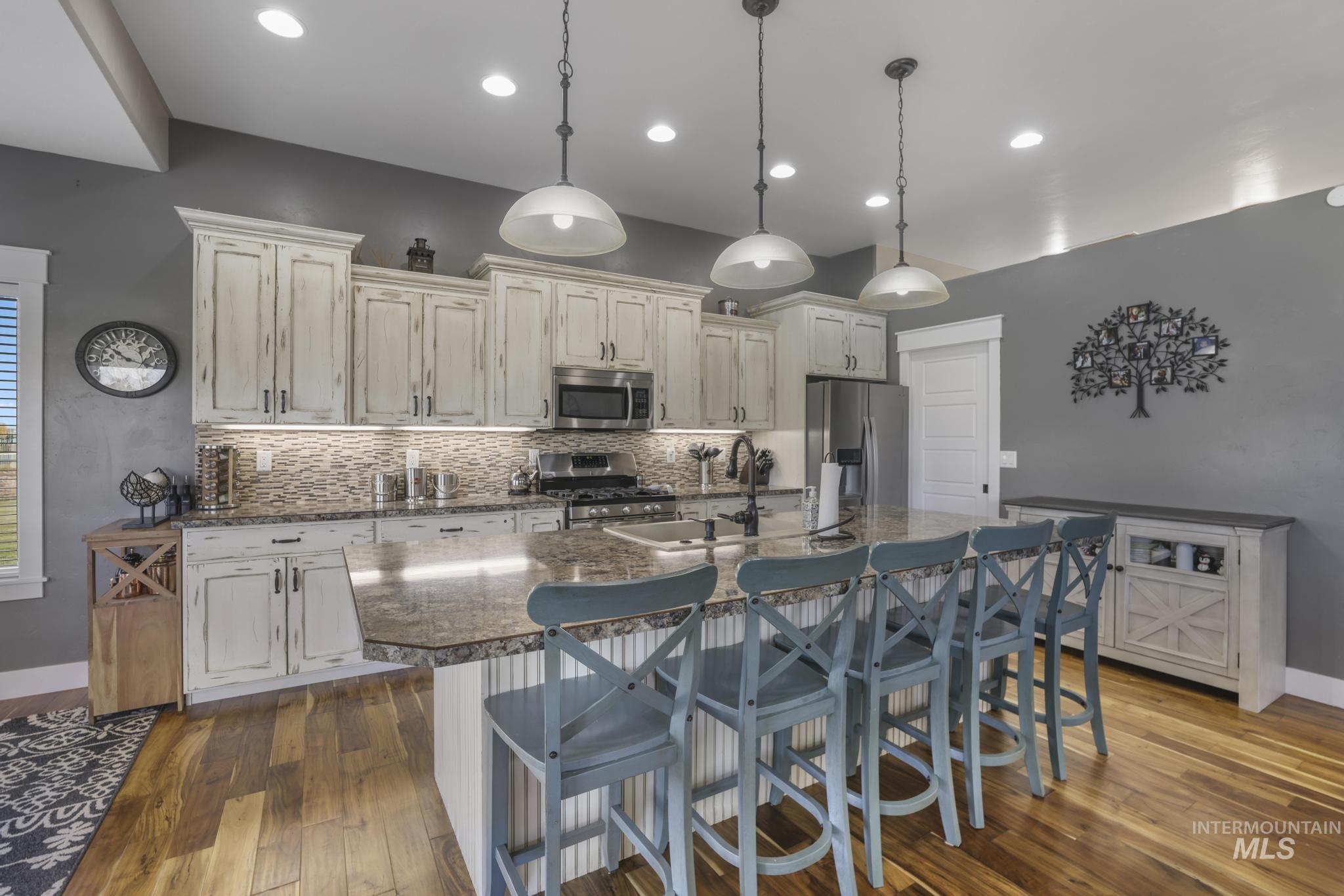 Kitchen featuring a kitchen breakfast bar, stainless steel appliances, dark wood-type flooring, a center island with sink, and hanging light fixtures