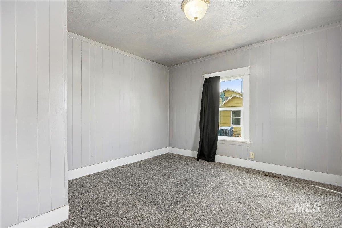 Empty room with carpet, crown molding, wood walls, and a textured ceiling