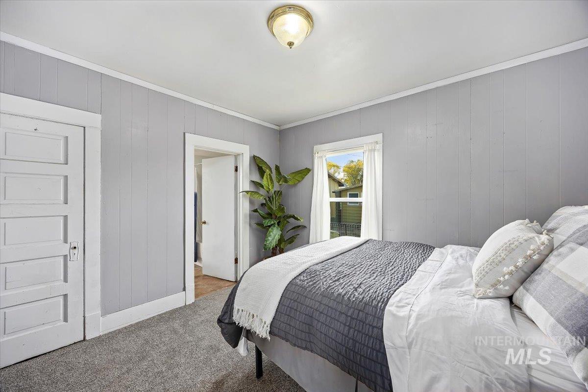Bedroom with crown molding, wooden walls, and carpet flooring