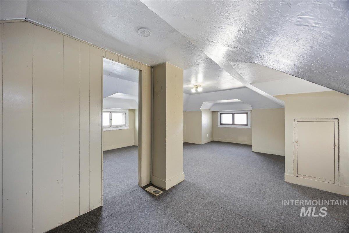 Bonus room with a textured ceiling, dark carpet, plenty of natural light, and vaulted ceiling