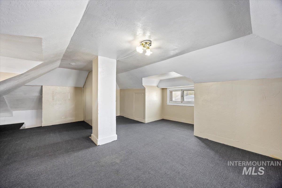 Additional living space with dark colored carpet, a textured ceiling, and lofted ceiling