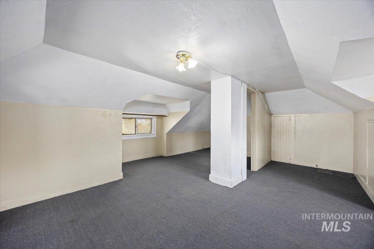Additional living space with dark colored carpet, a textured ceiling, and vaulted ceiling