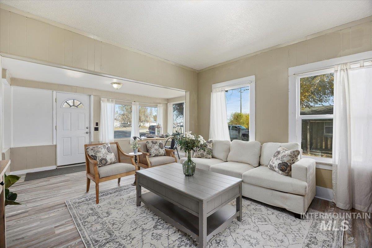 Living room featuring light wood-style flooring, wood walls, a textured ceiling, and ornamental molding