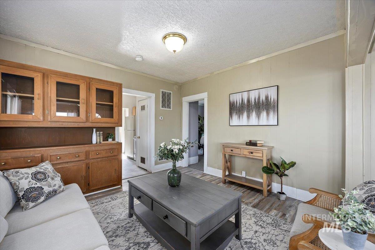 Living area with light wood-type flooring, crown molding, a textured ceiling, and wooden walls