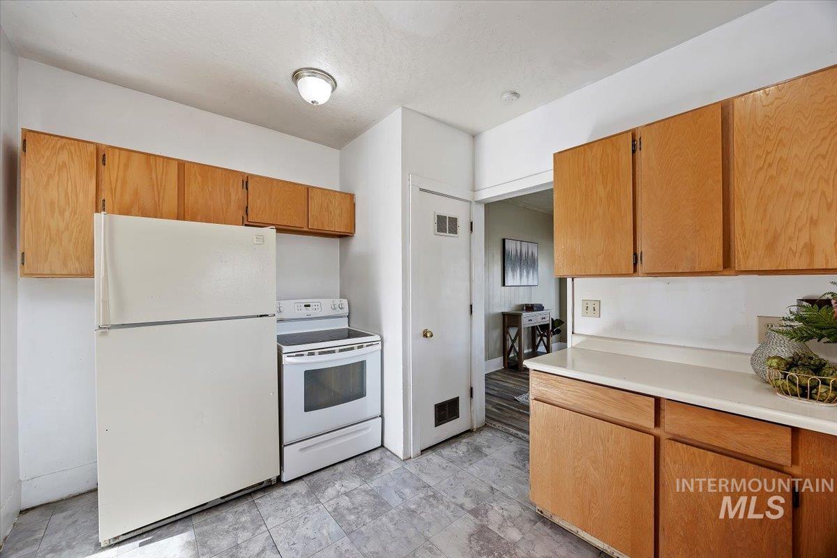 Kitchen with white appliances, light countertops, brown cabinetry, and a textured ceiling