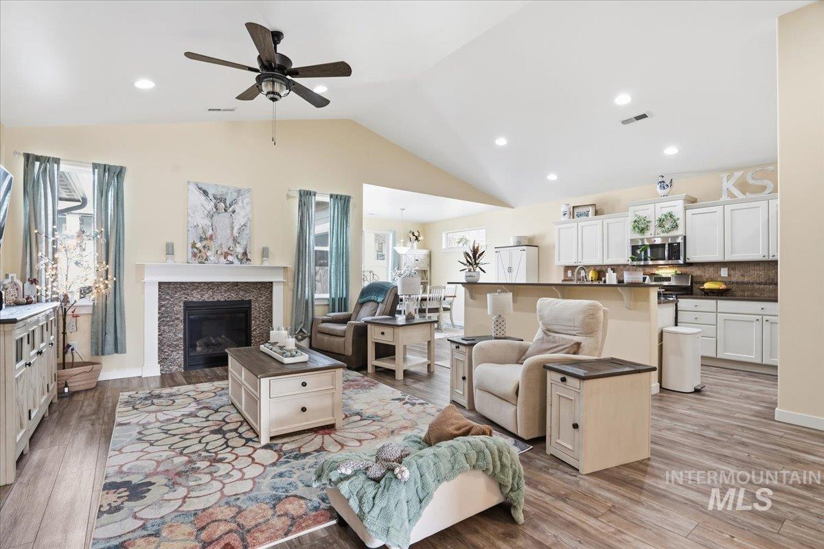 Living area featuring ceiling fan, lofted ceiling, light wood-type flooring, a tile fireplace, and recessed lighting