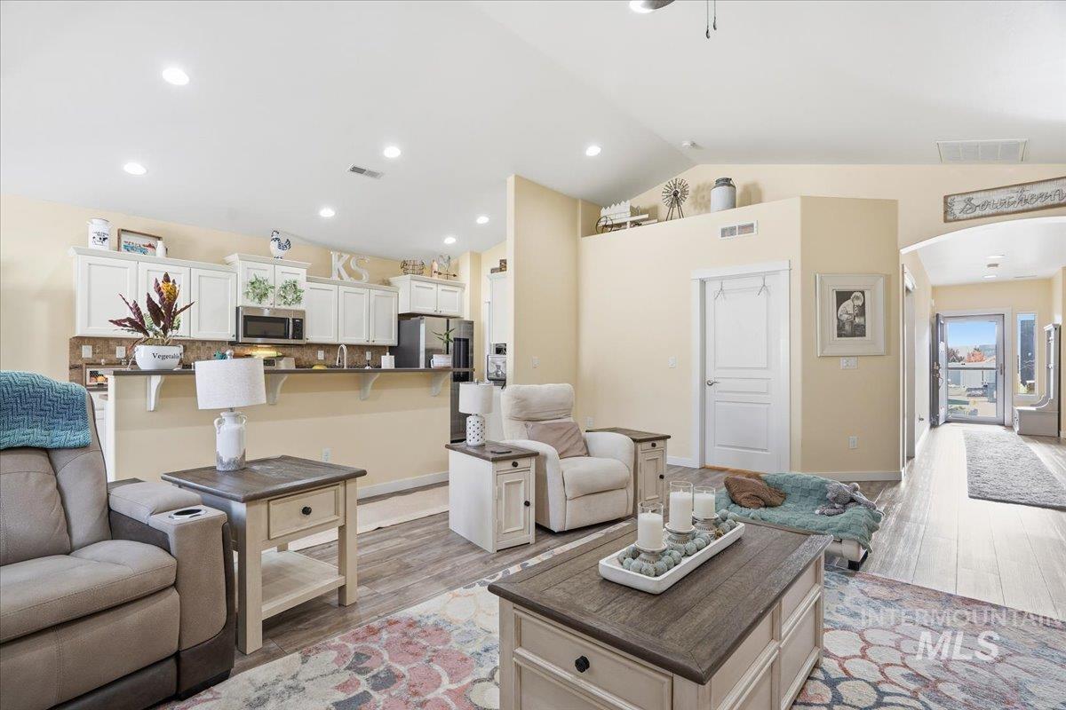 Living area featuring light wood-style flooring, lofted ceiling, arched walkways, and recessed lighting