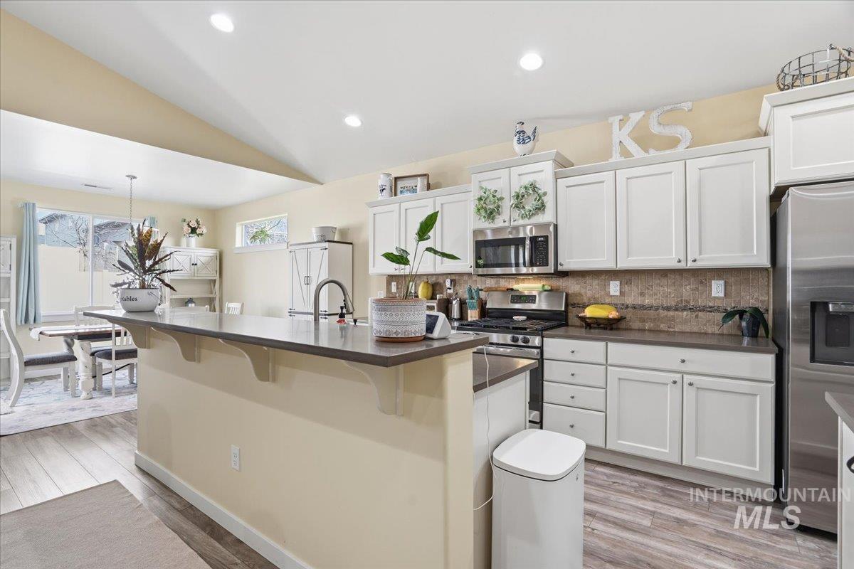 Kitchen featuring decorative backsplash, white cabinets, stainless steel appliances, decorative light fixtures, and lofted ceiling