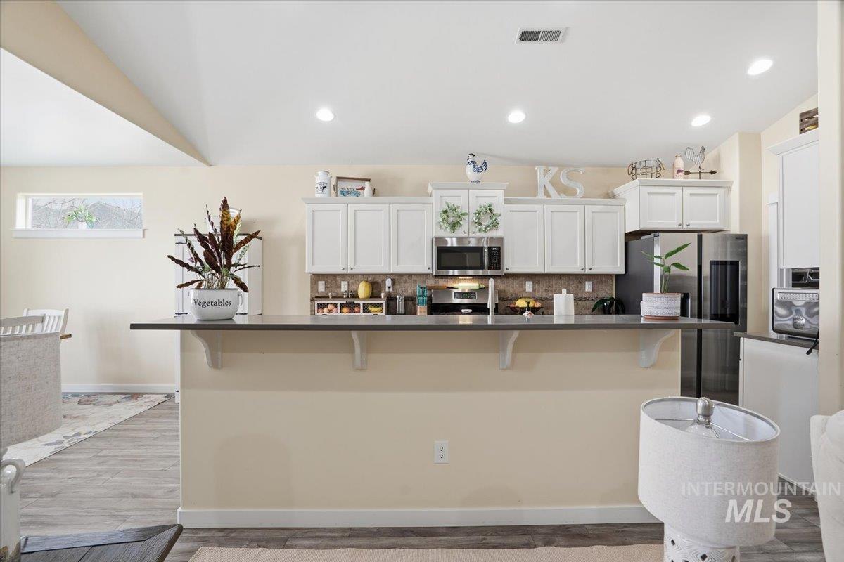 Kitchen featuring a kitchen bar, tasteful backsplash, white cabinetry, dark countertops, and recessed lighting