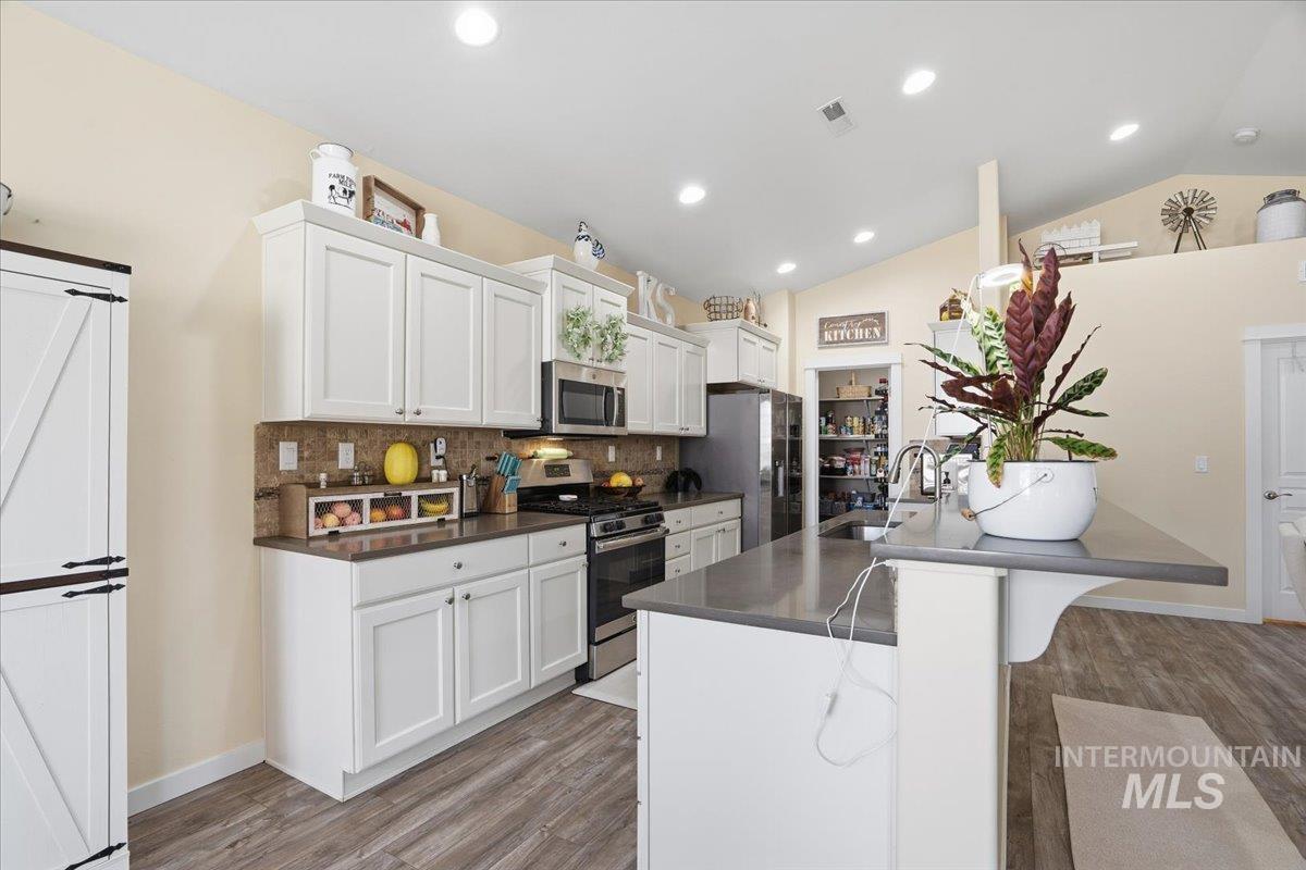 Kitchen featuring appliances with stainless steel finishes, decorative backsplash, white cabinets, light wood-style floors, and lofted ceiling