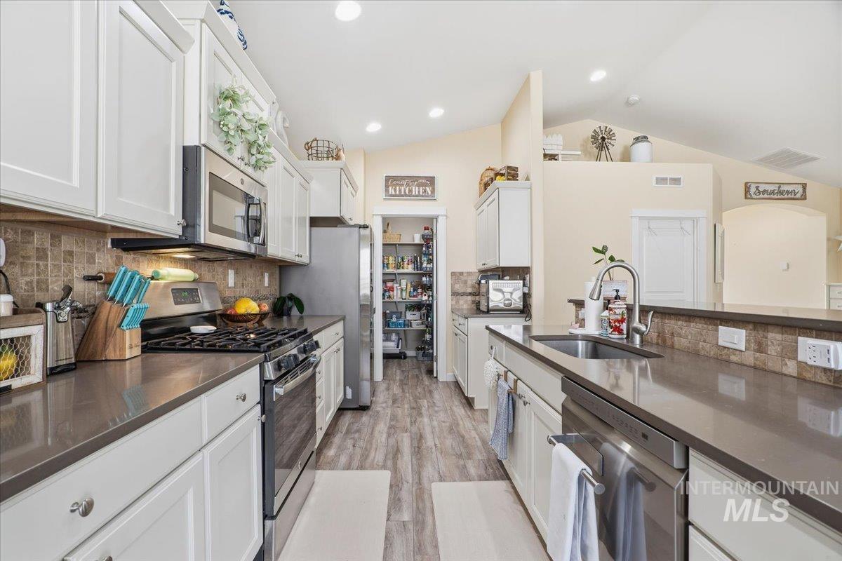 Kitchen with stainless steel appliances, decorative backsplash, white cabinets, light wood finished floors, and vaulted ceiling
