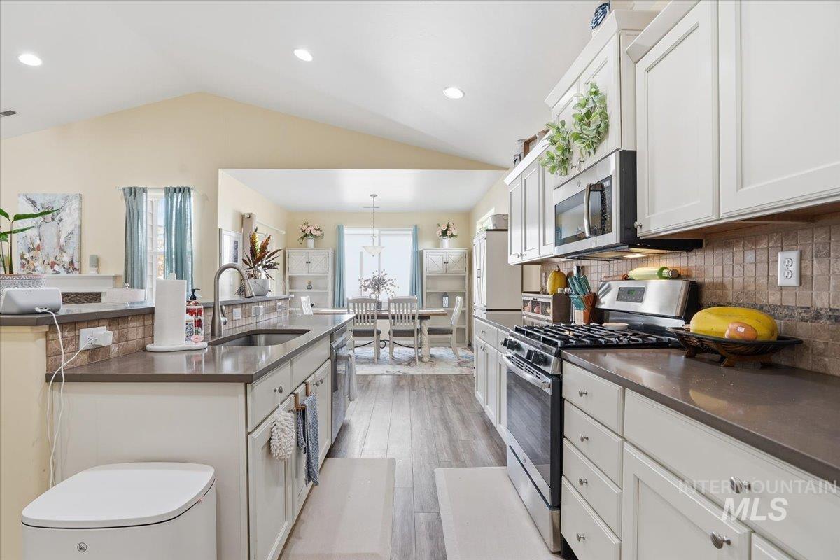 Kitchen featuring white cabinets, stainless steel appliances, backsplash, light wood-style floors, and lofted ceiling