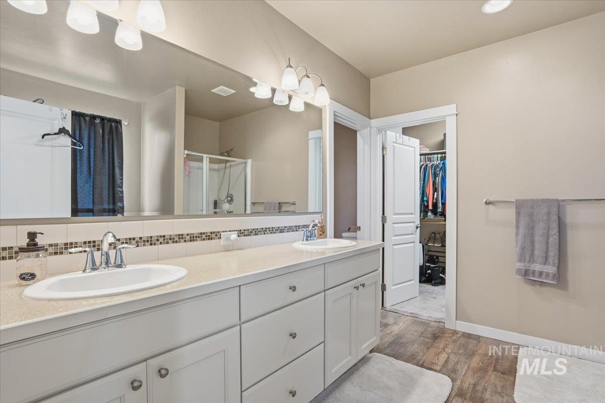Bathroom with double vanity, a stall shower, dark wood-type flooring, a spacious closet, and tasteful backsplash
