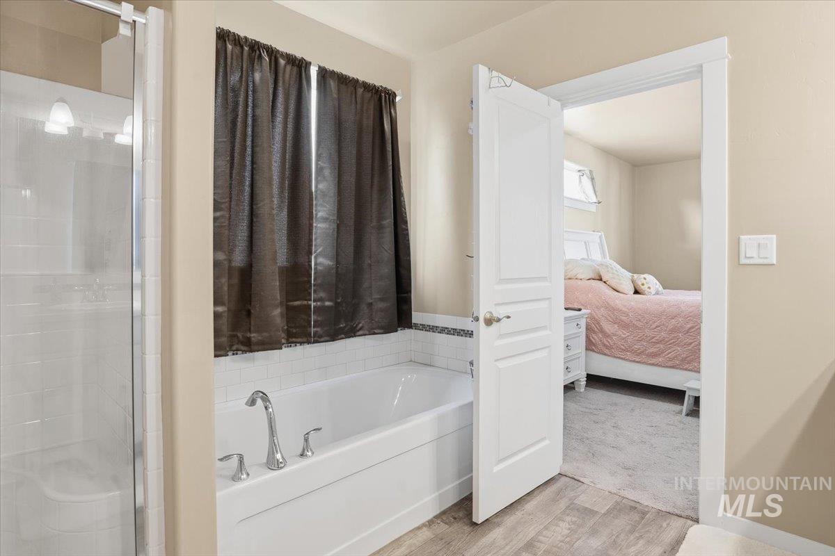 Ensuite bathroom with light wood-type flooring, a bath, and a stall shower