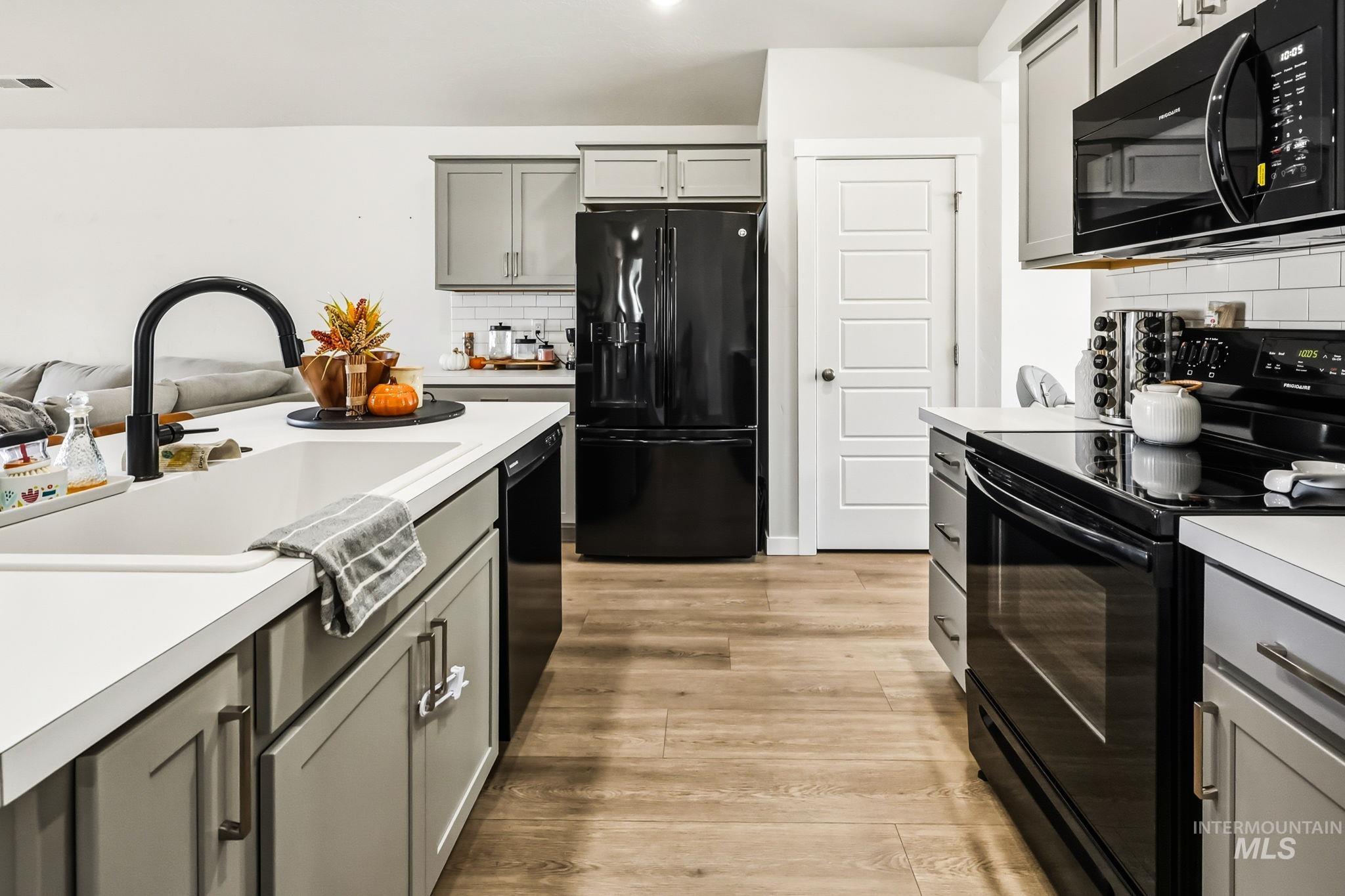 Kitchen featuring black appliances, gray cabinetry, light countertops, backsplash, and light wood finished floors
