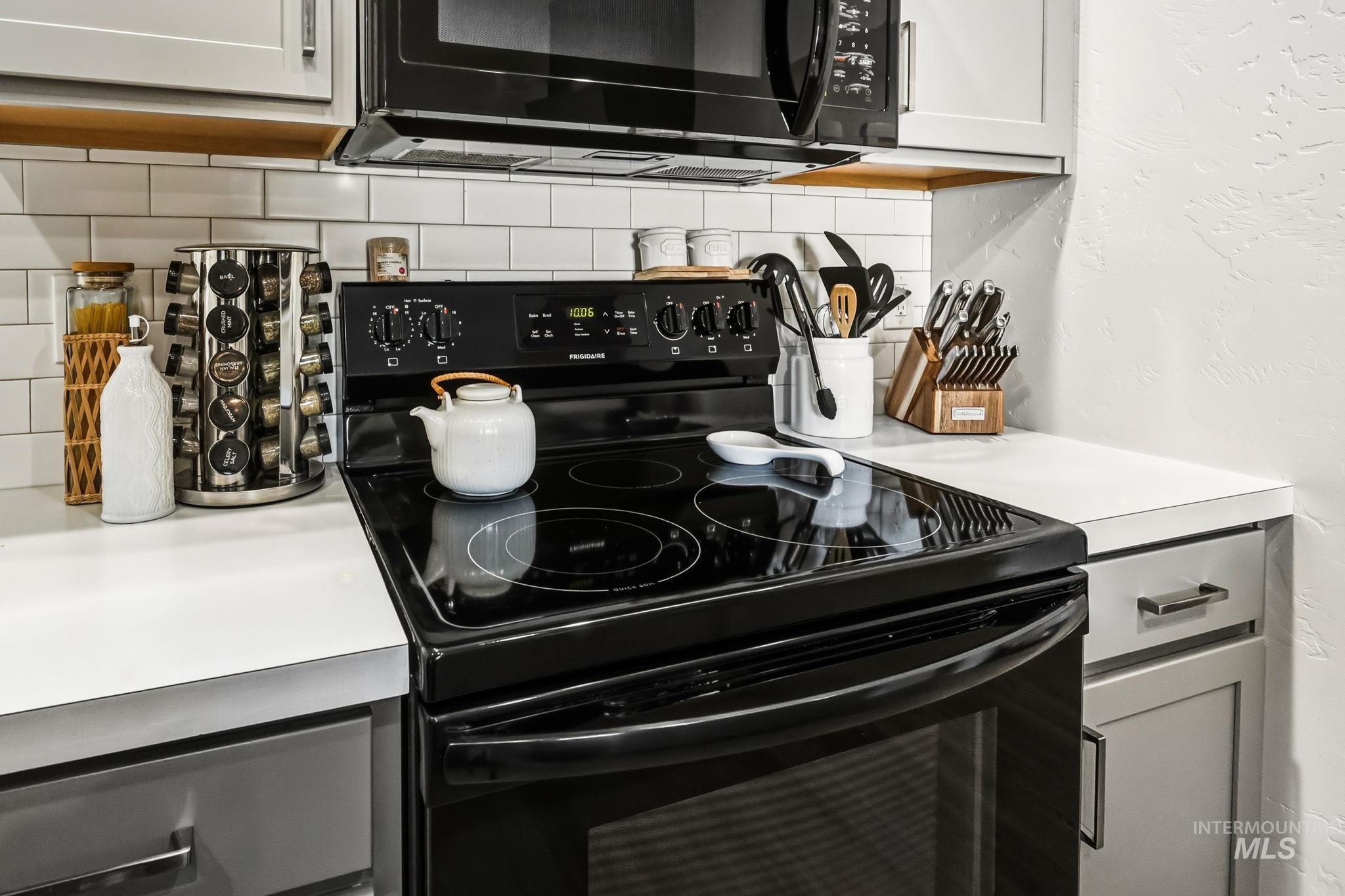 Kitchen with black appliances, light countertops, decorative backsplash, and a textured wall