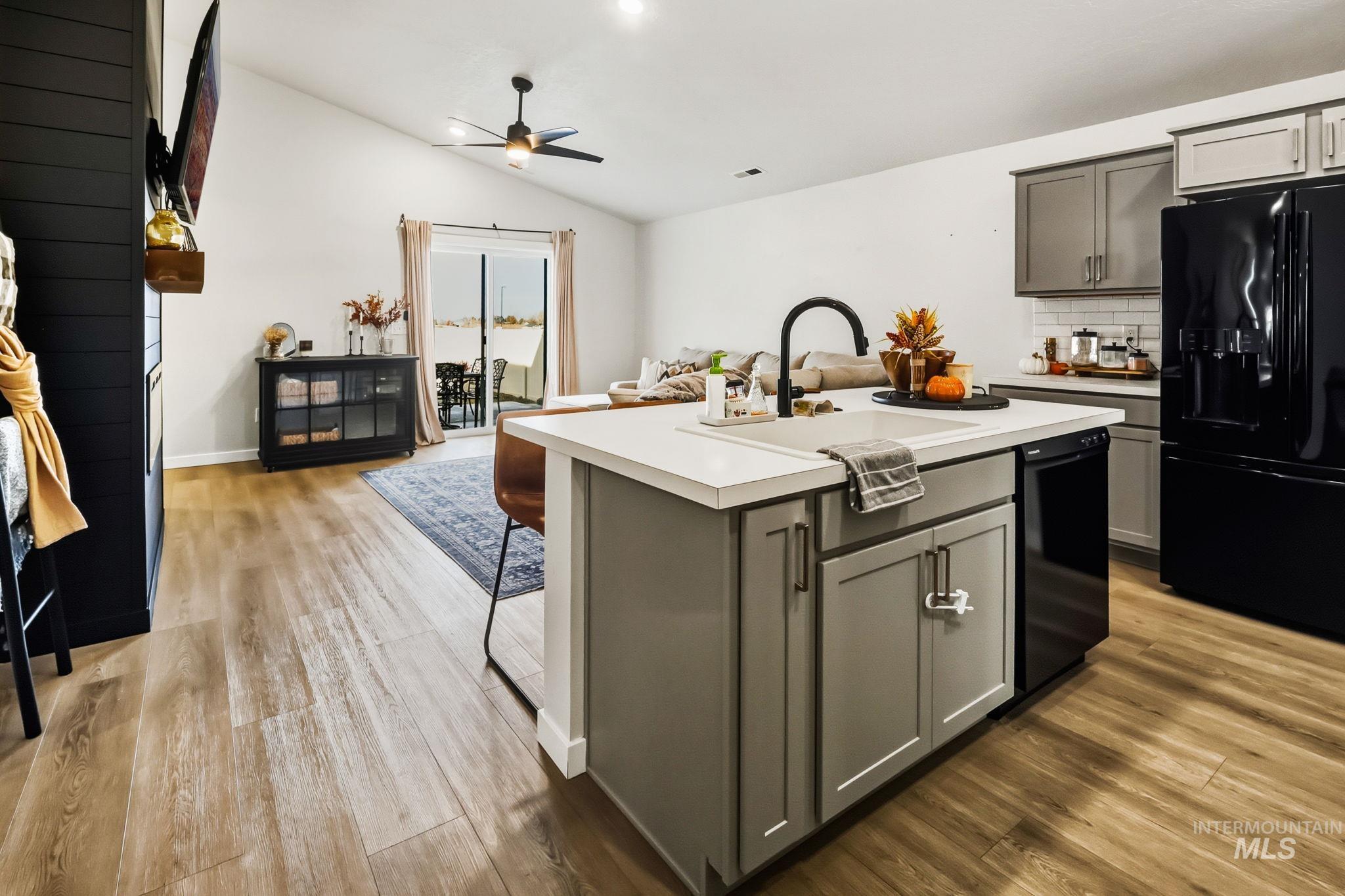 Kitchen with decorative backsplash, a kitchen island with sink, black appliances, light countertops, and lofted ceiling