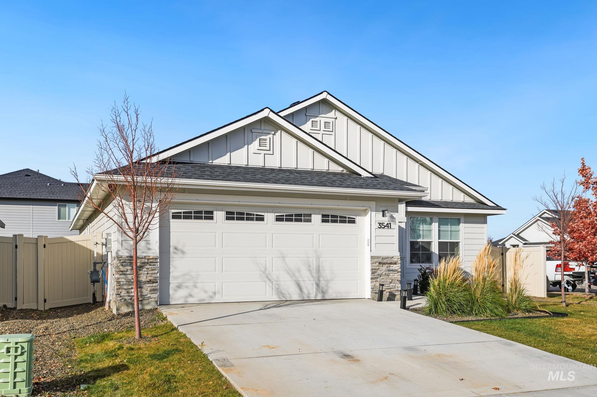 View of front of home with board and batten siding, a shingled roof, concrete driveway, stone siding, and a gate