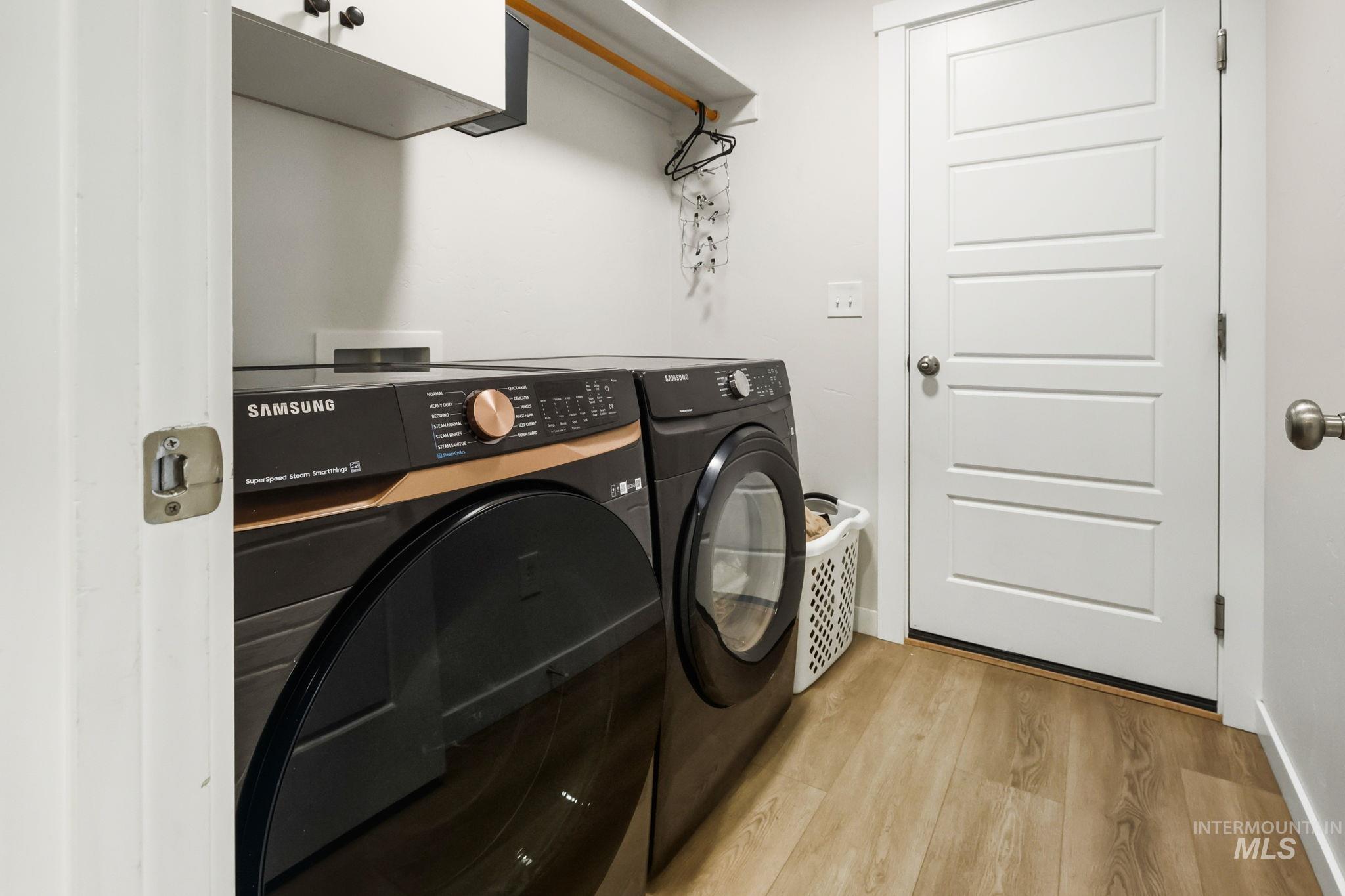 Washroom with light wood-type flooring and washing machine and clothes dryer