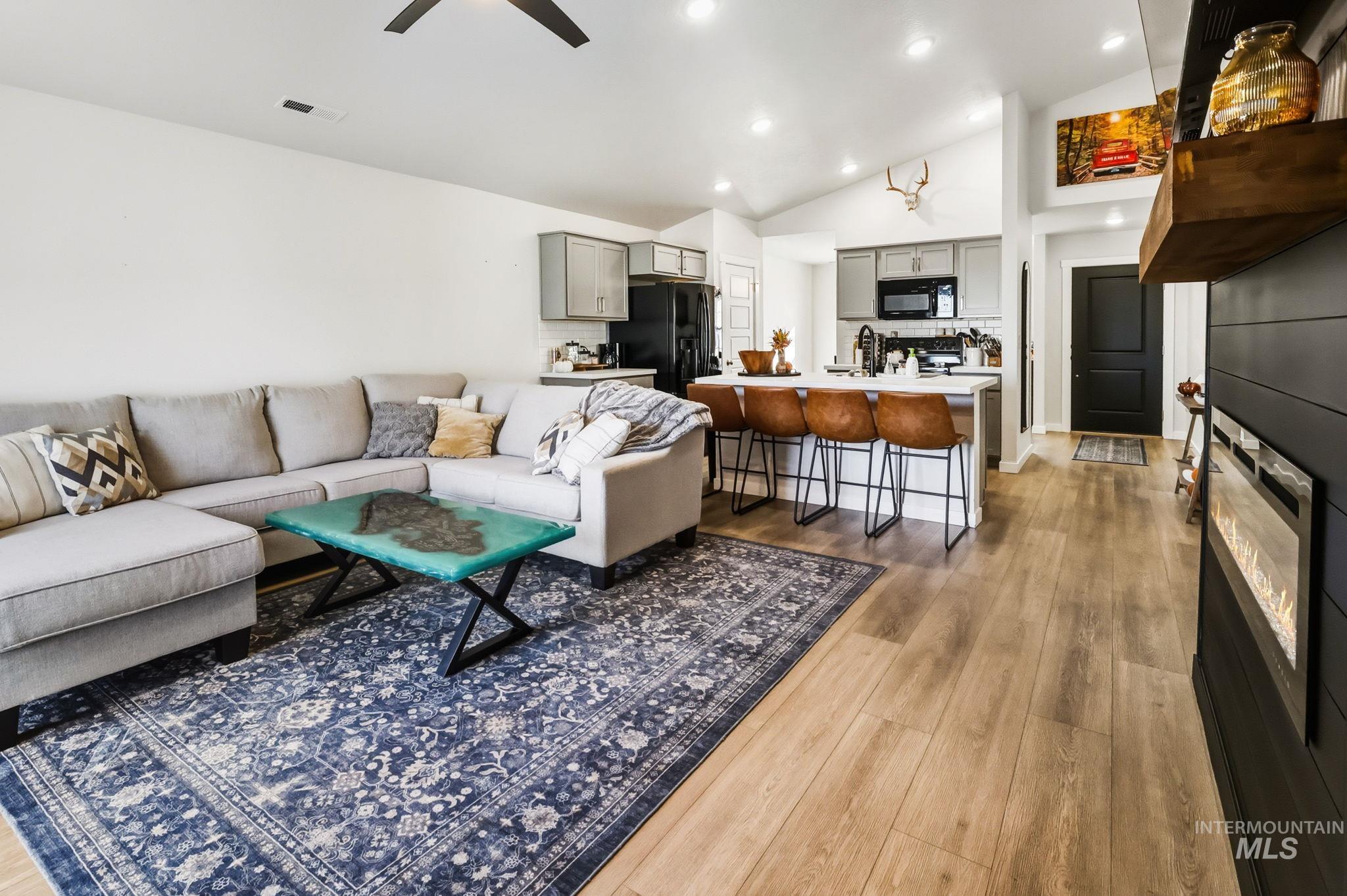 Living room with light wood finished floors, recessed lighting, a ceiling fan, a glass covered fireplace, and high vaulted ceiling