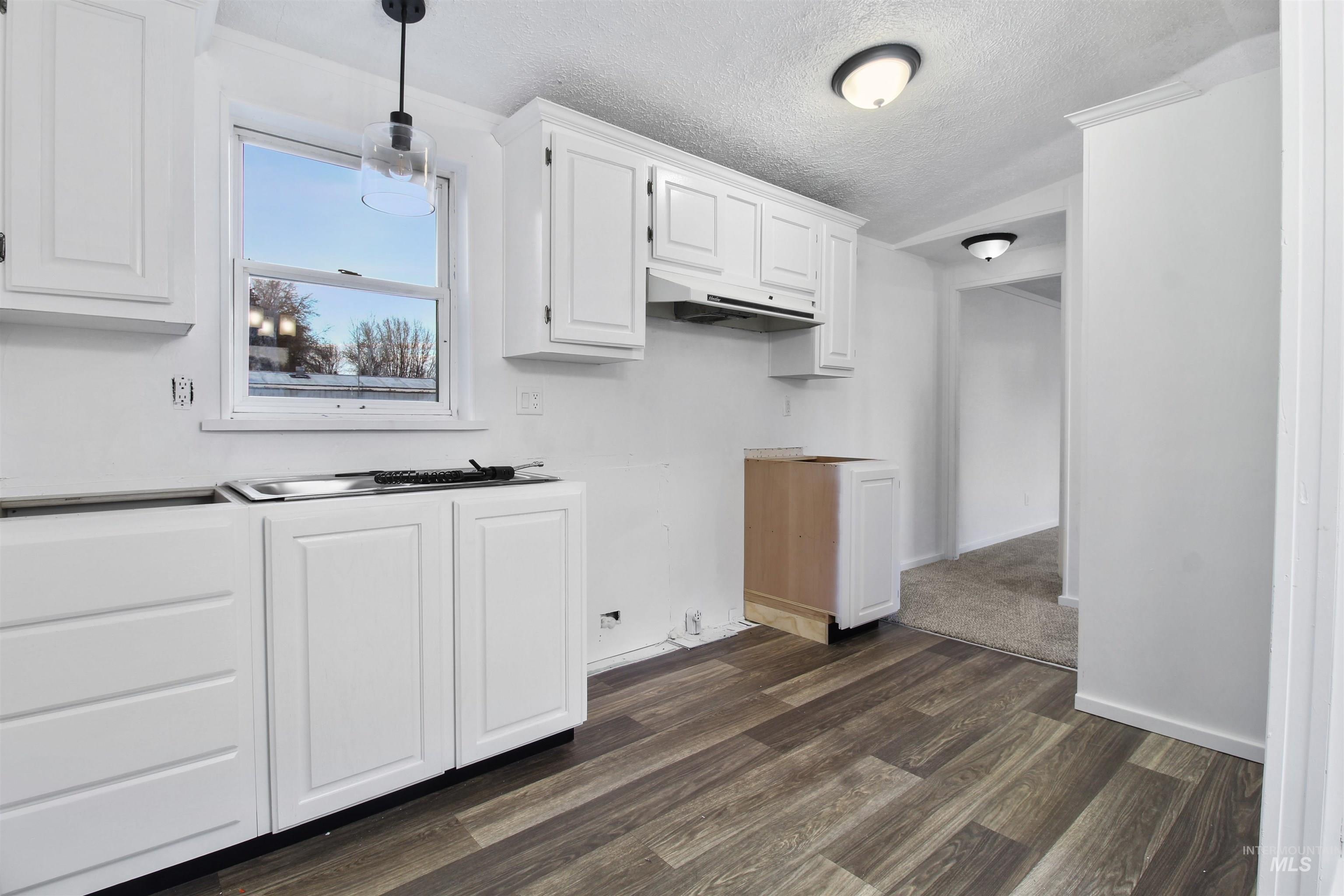 Kitchen with white cabinets, dark wood finished floors, a textured ceiling, pendant lighting, and under cabinet range hood