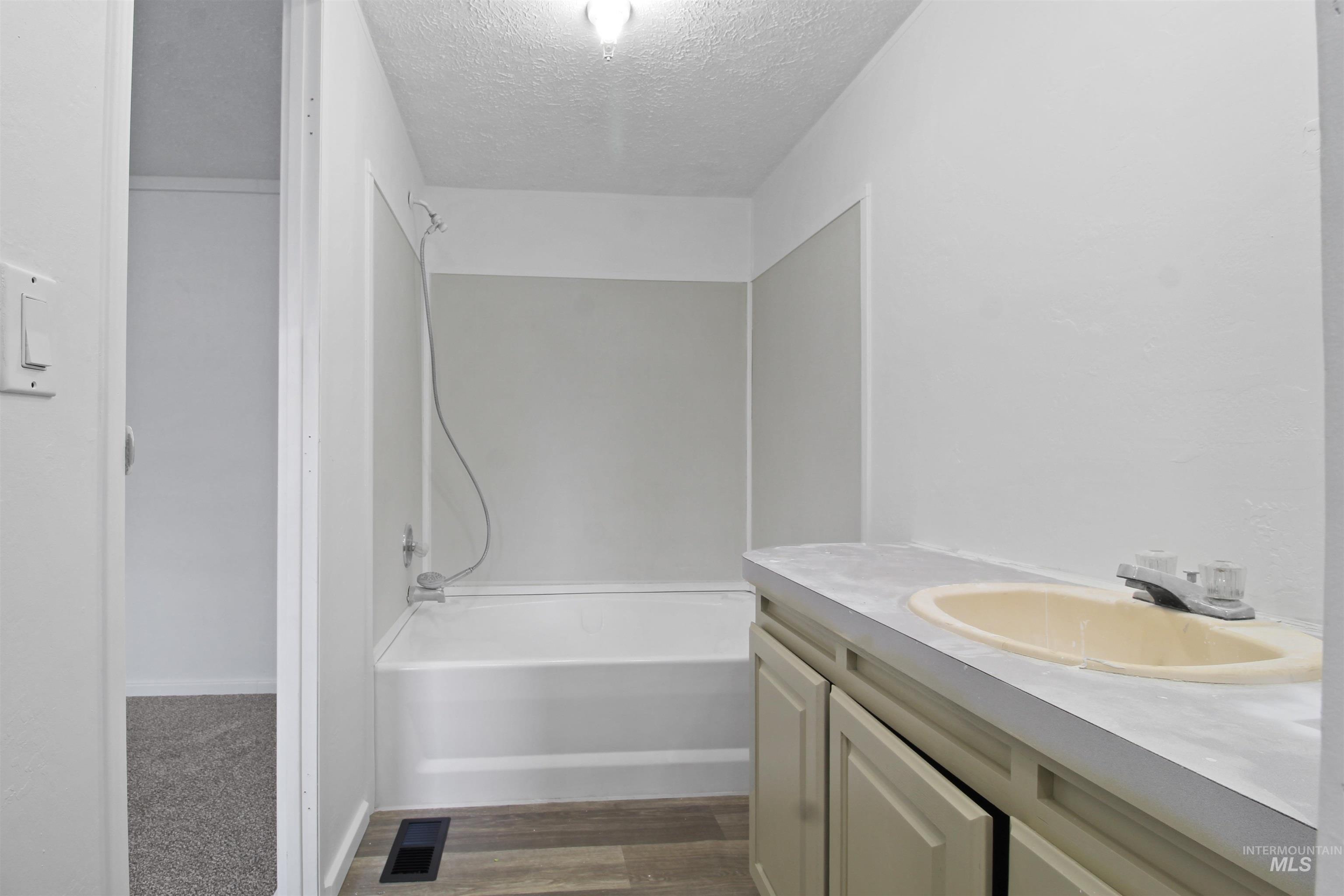 Full bath with a textured ceiling, vanity, shower / bath combination, and dark wood finished floors