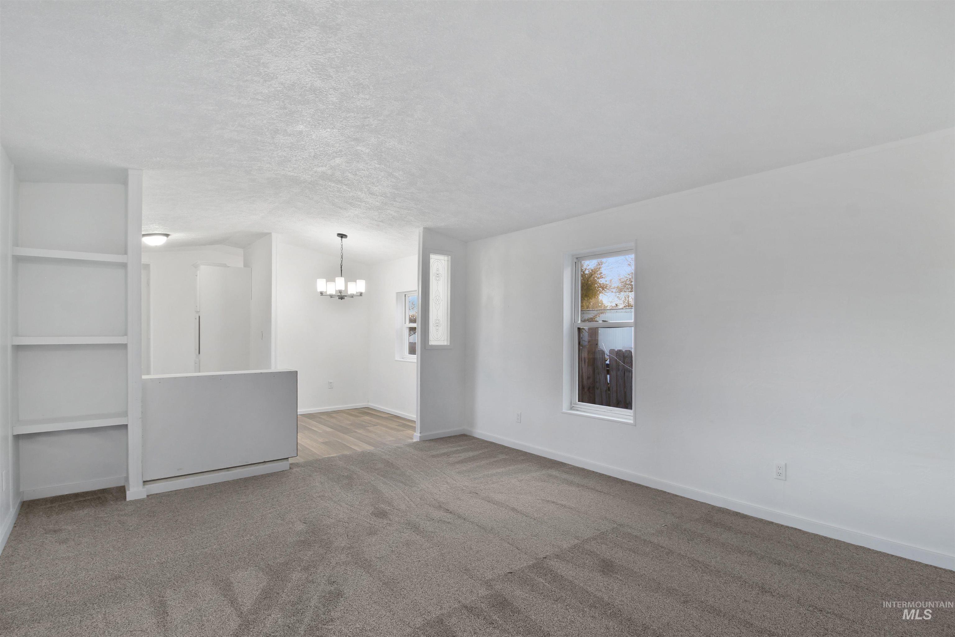 Carpeted empty room featuring a textured ceiling and a chandelier