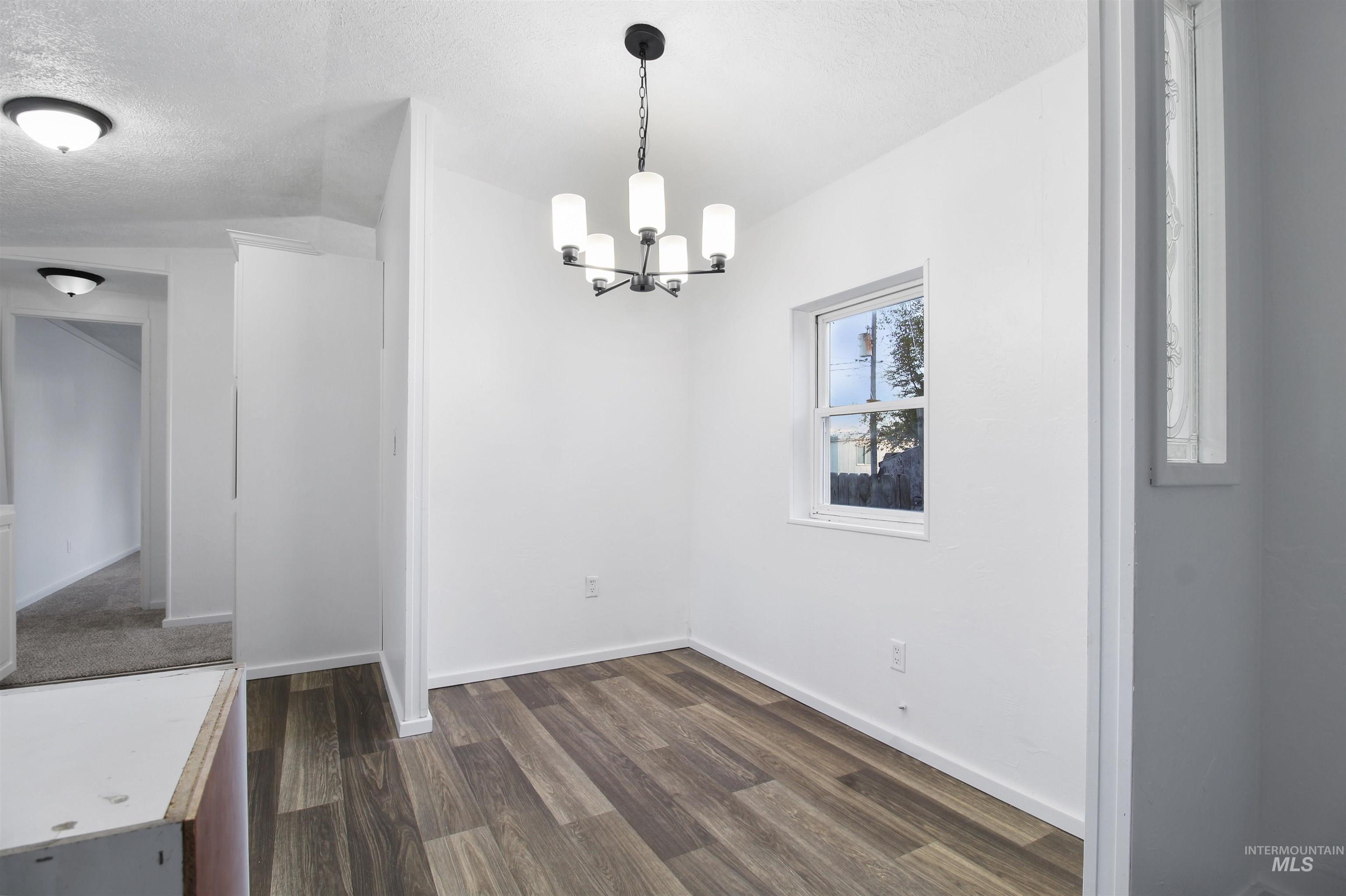 Unfurnished dining area featuring dark wood-style floors, a textured ceiling, and a chandelier