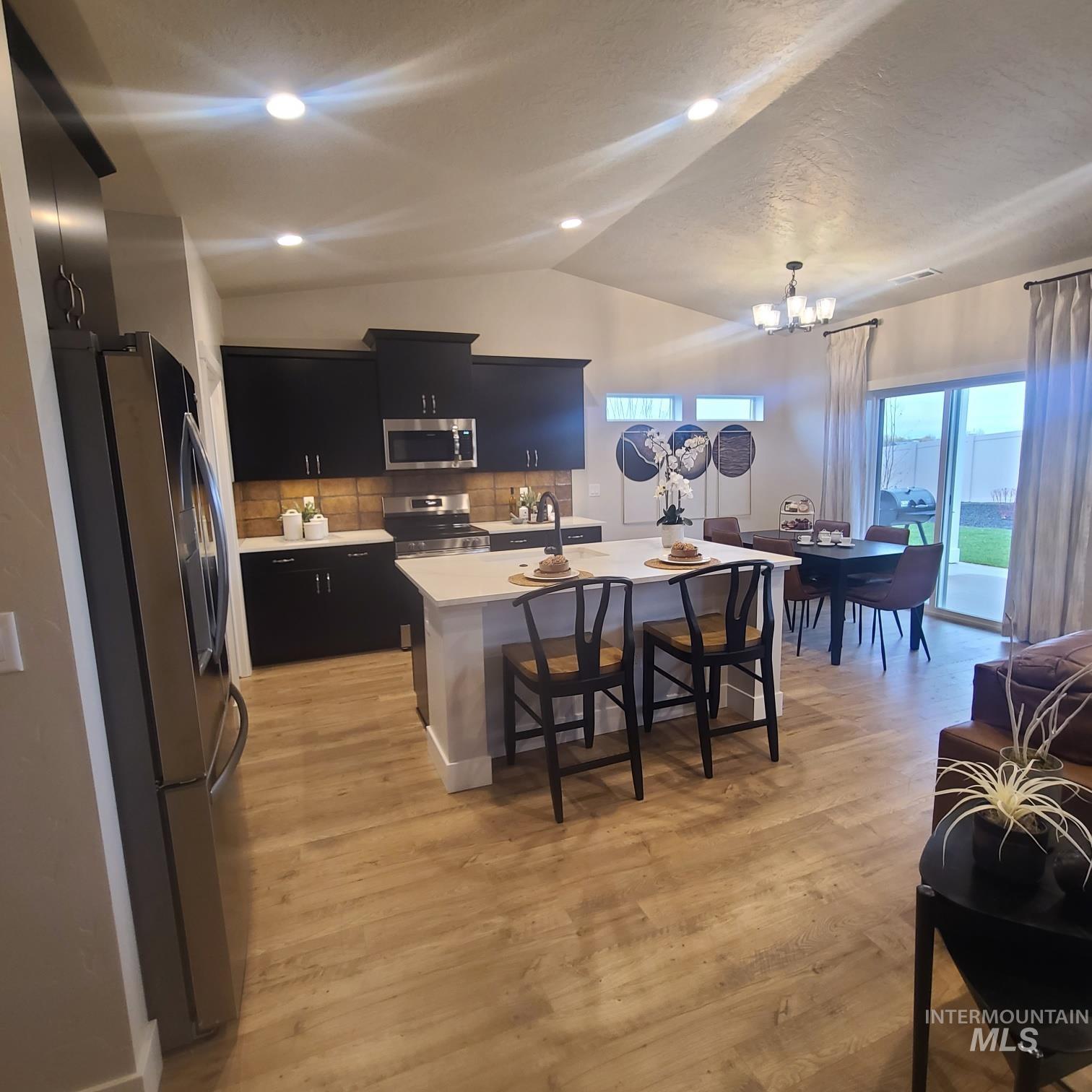 Kitchen with dark cabinets, lofted ceiling, appliances with stainless steel finishes, backsplash, and a kitchen island with sink