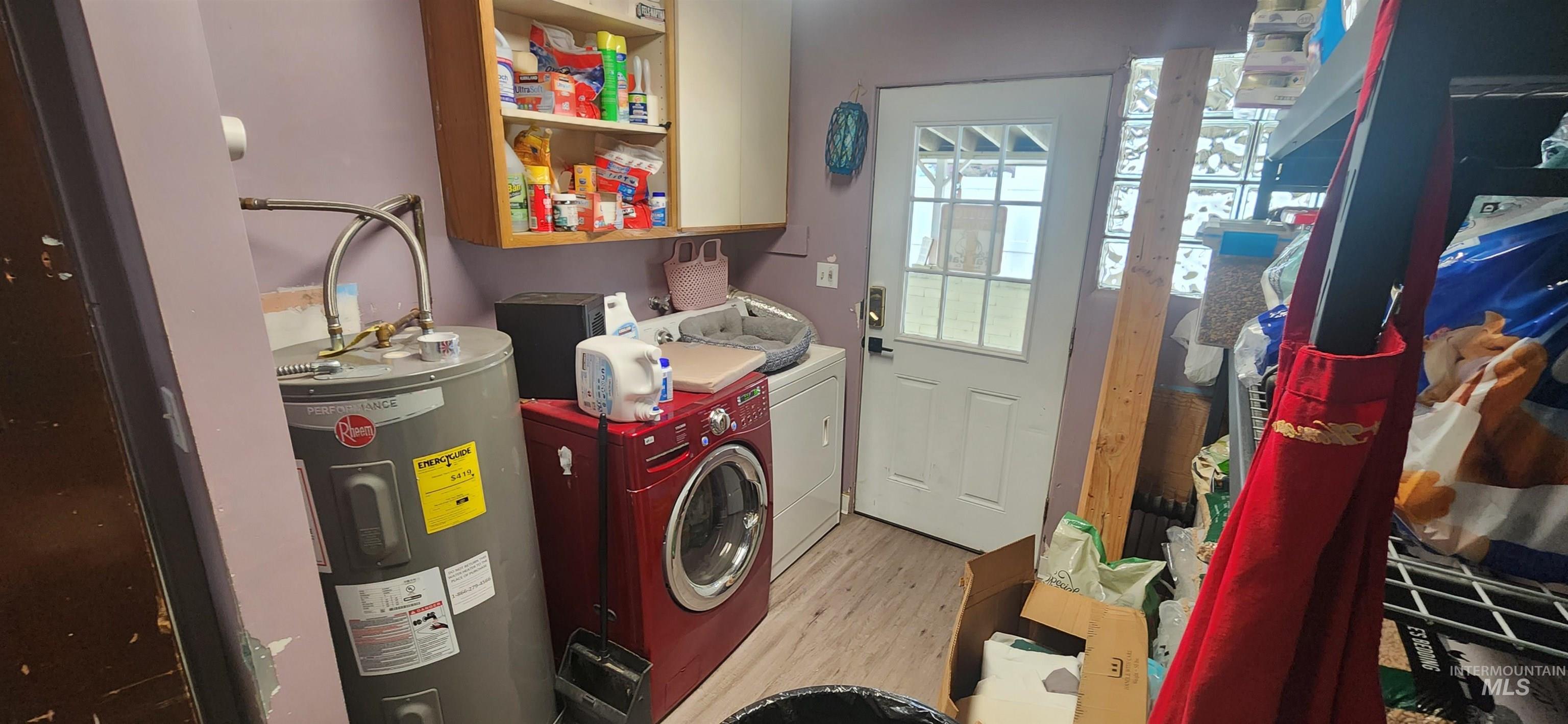 Laundry area with water heater, washer and dryer, and light wood-style flooring