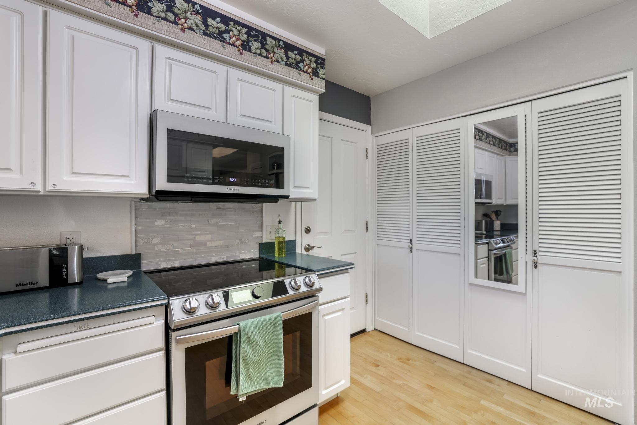 Kitchen with dark countertops, appliances with stainless steel finishes, white cabinetry, tasteful backsplash, and light wood-style flooring