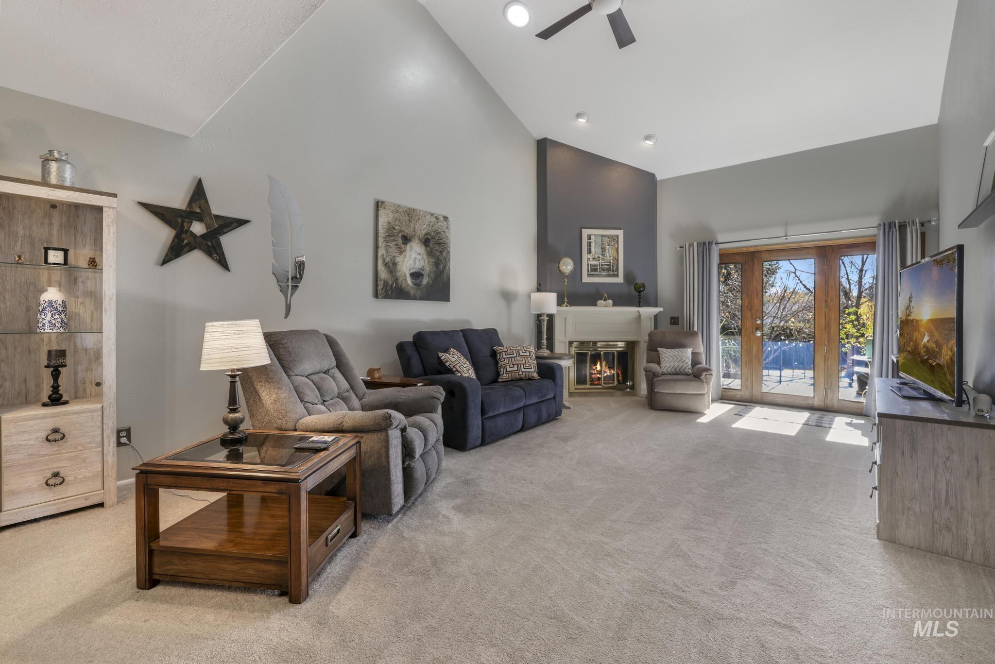 Living room featuring high vaulted ceiling, light colored carpet, a glass covered fireplace, and a ceiling fan