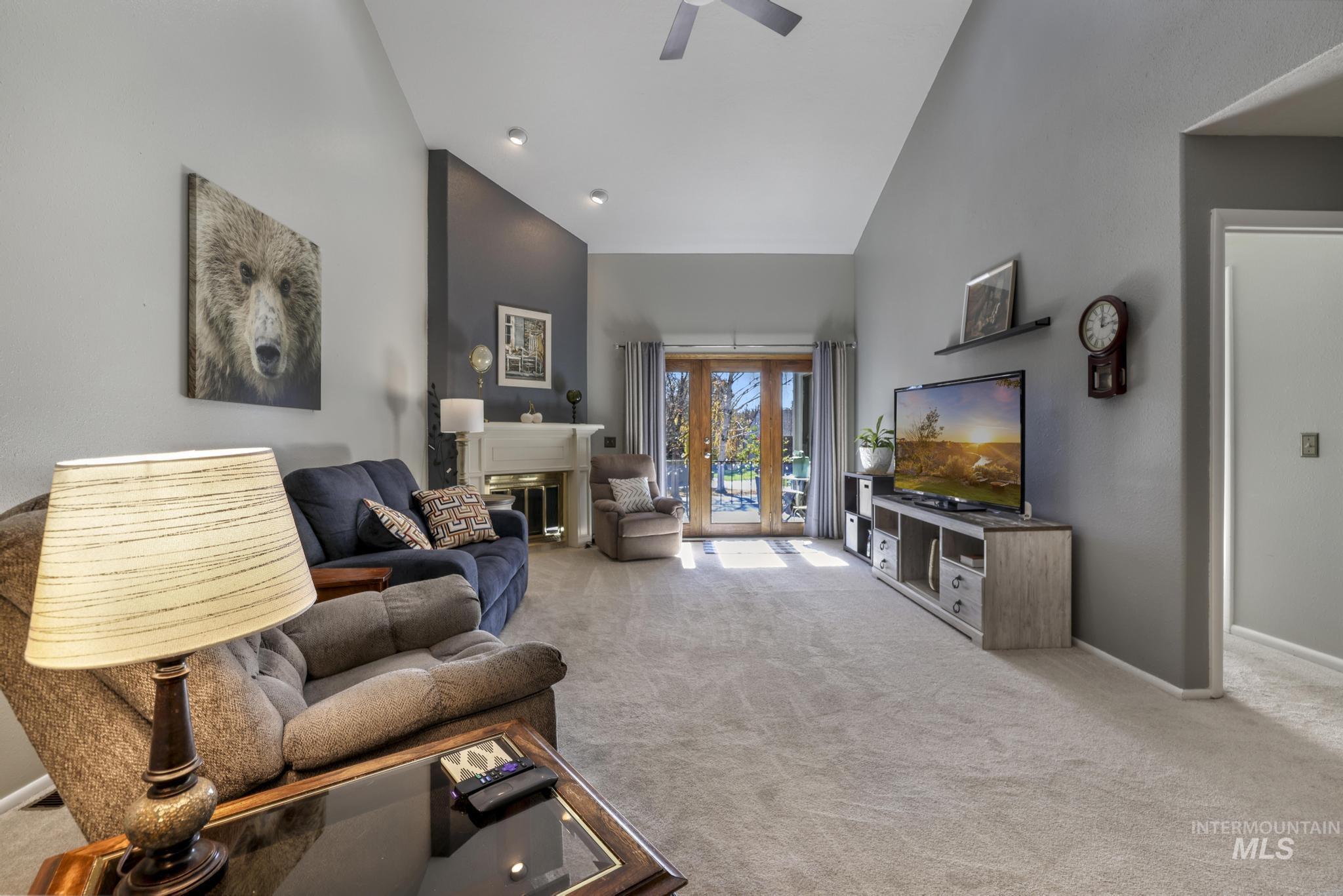 Living area with a fireplace, light carpet, high vaulted ceiling, and a ceiling fan