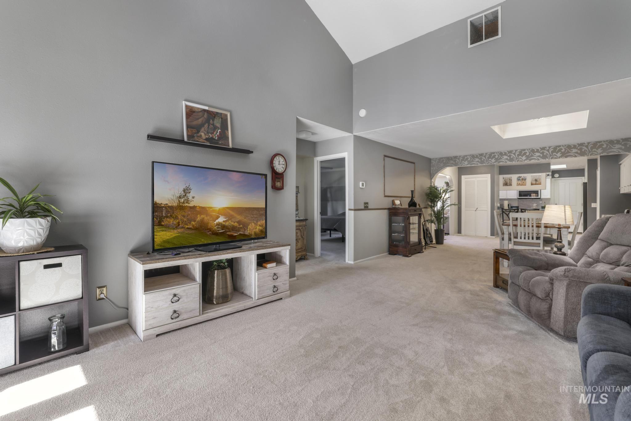 Living room with light carpet, a skylight, and a towering ceiling