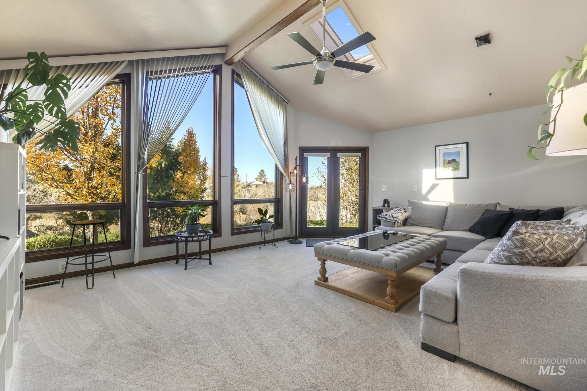Living room with beam ceiling, light colored carpet, high vaulted ceiling, a skylight, and a ceiling fan