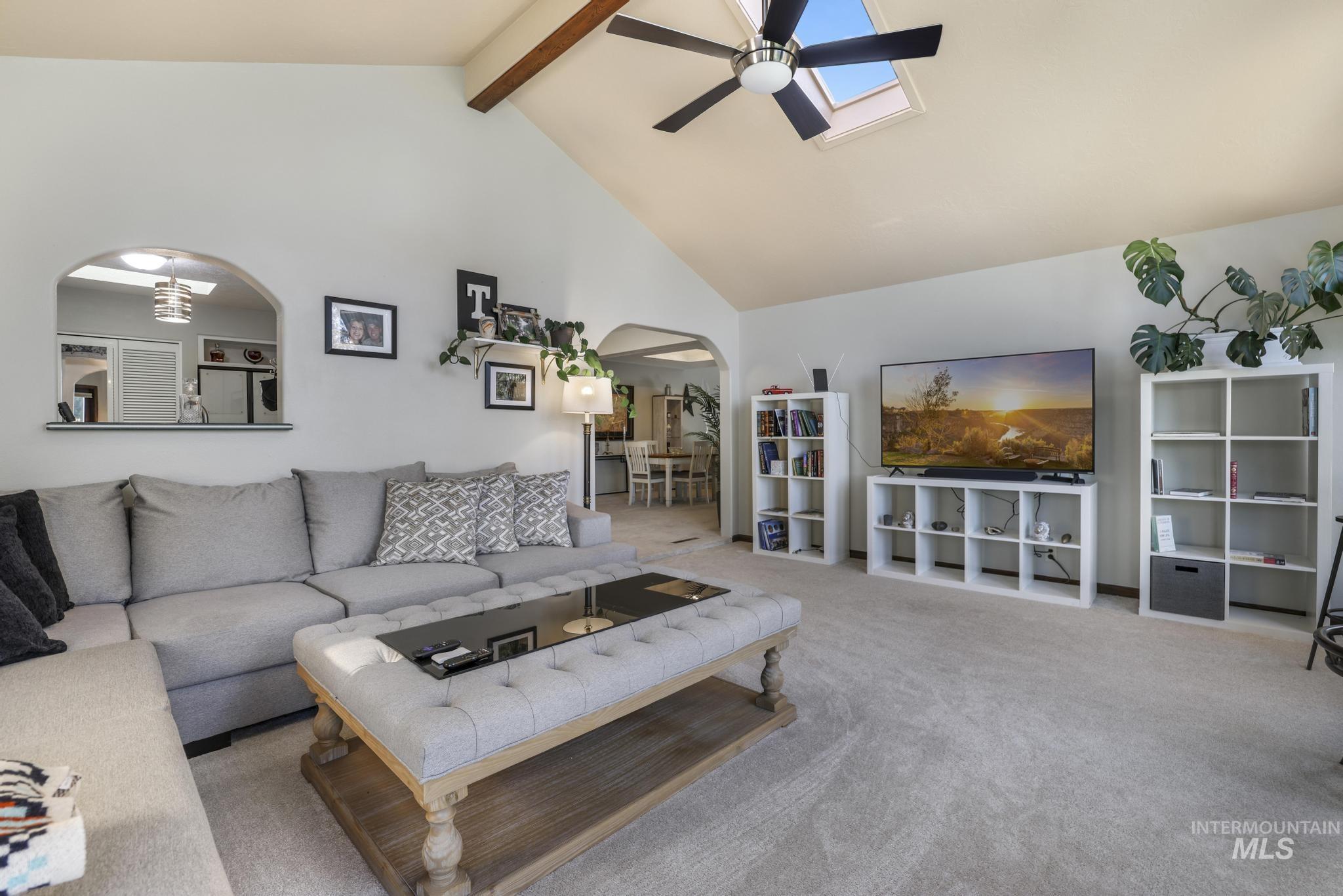Living area with high vaulted ceiling, arched walkways, beam ceiling, a skylight, and carpet floors