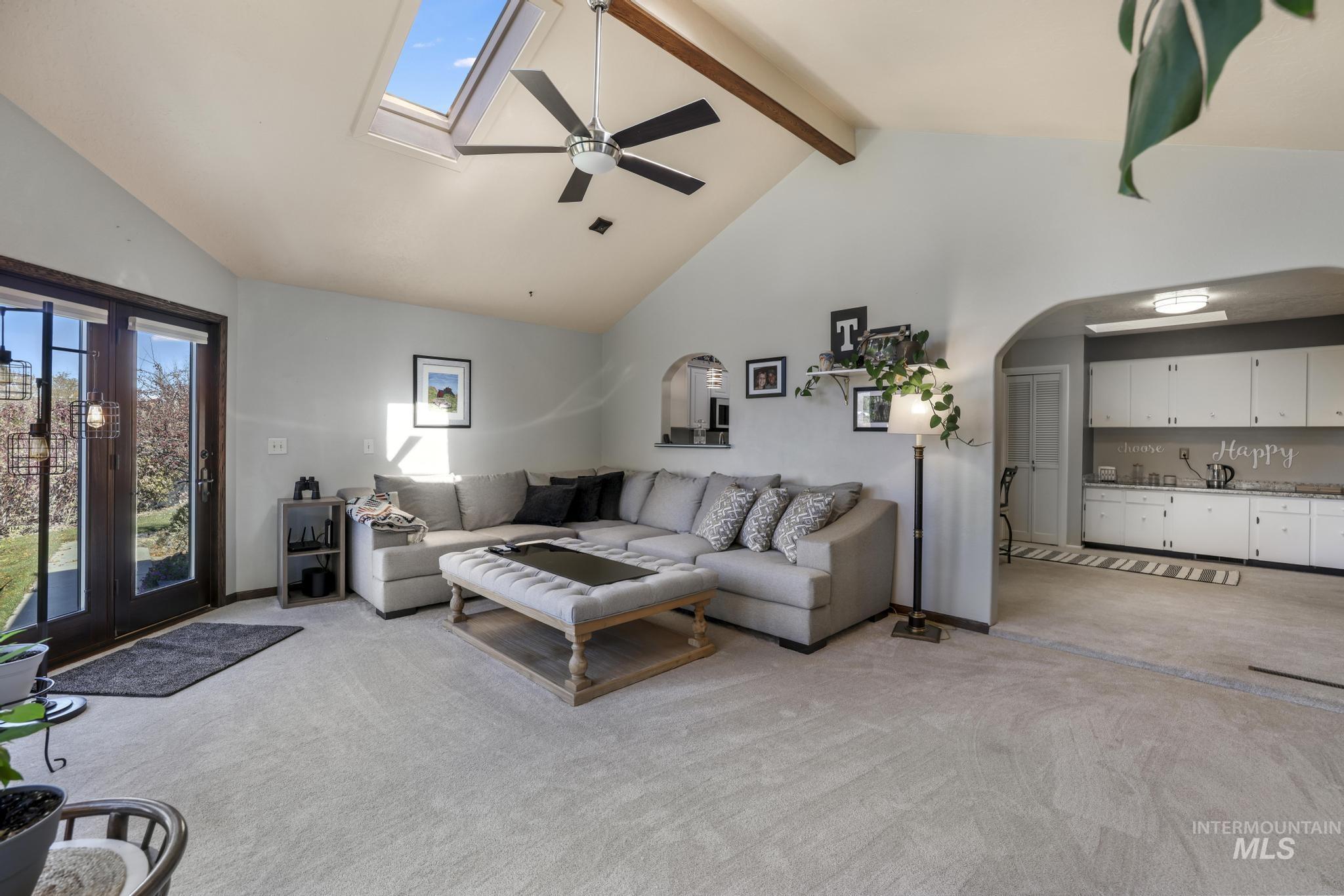 Living area with carpet, high vaulted ceiling, a skylight, ceiling fan, and beamed ceiling