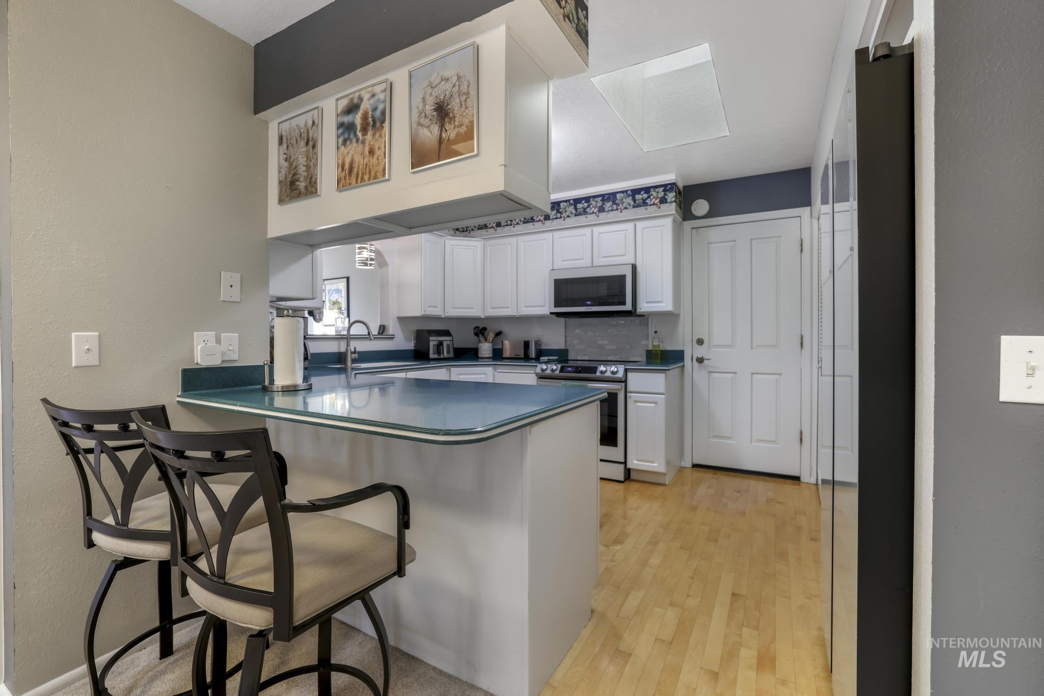 Kitchen with white cabinetry, a peninsula, a breakfast bar area, stainless steel electric stove, and freestanding refrigerator