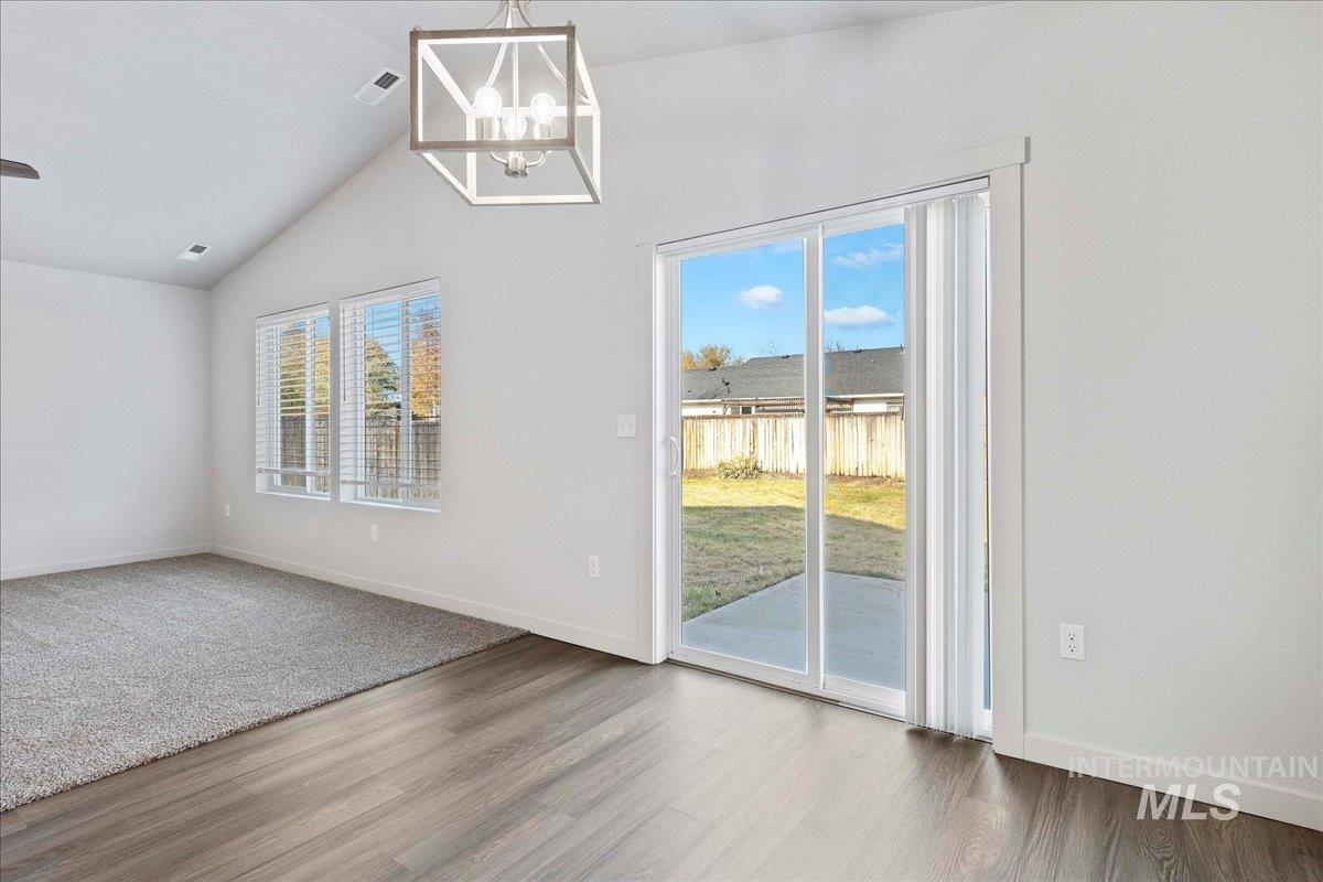 Unfurnished dining area with healthy amount of natural light, lofted ceiling, a chandelier, and wood finished floors