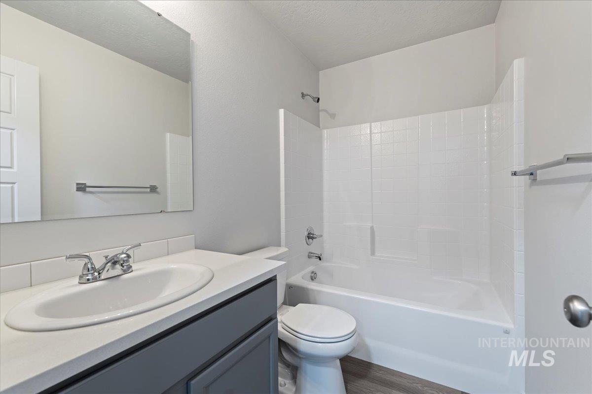 Full bathroom featuring vanity, bathing tub / shower combination, a textured ceiling, and dark wood-type flooring