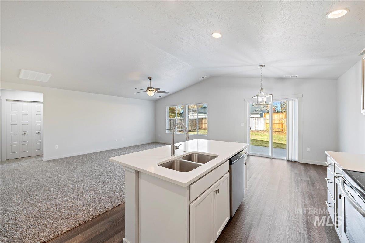 Kitchen featuring open floor plan, white cabinets, hanging light fixtures, a kitchen island with sink, and a textured ceiling