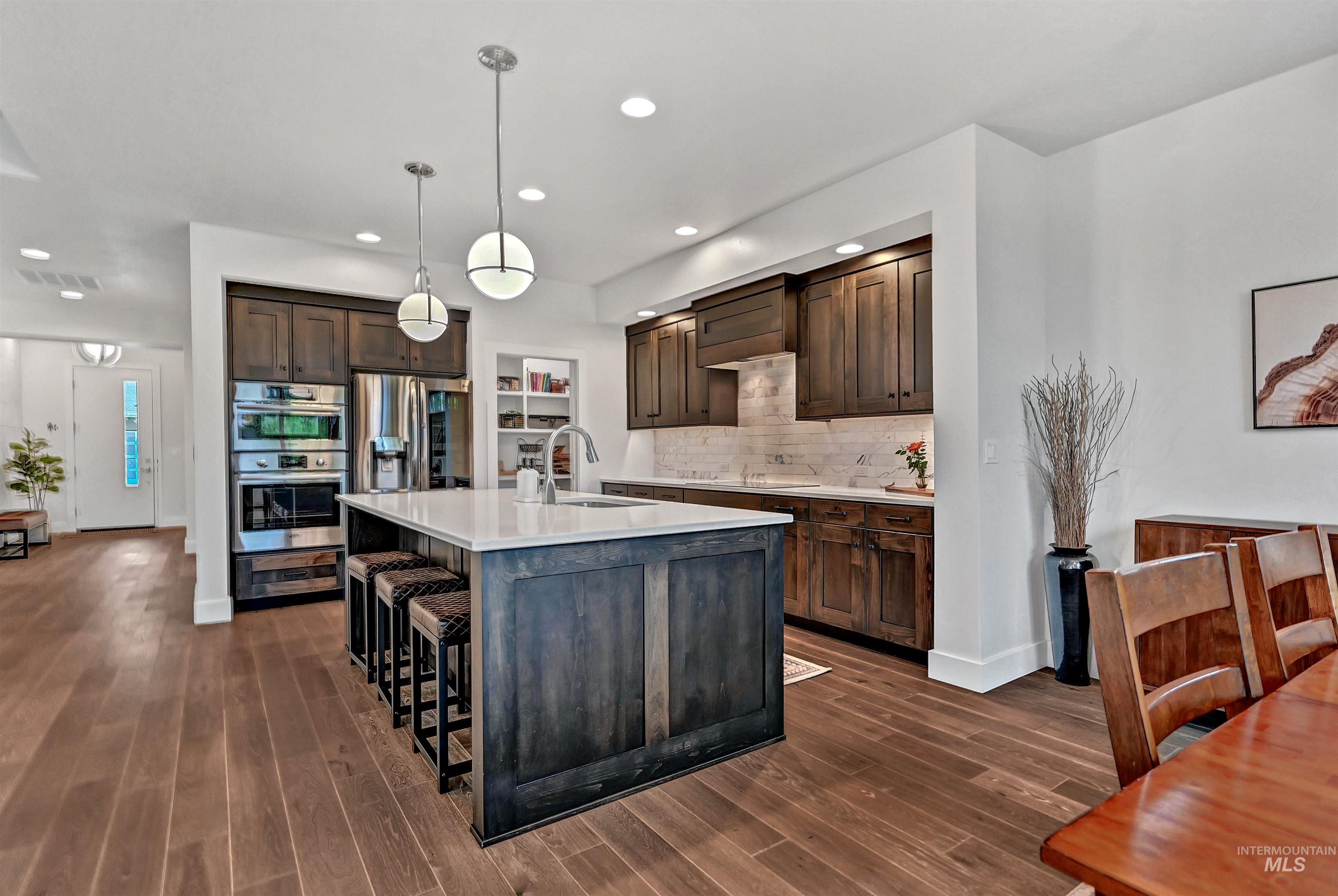 Kitchen with dark brown cabinets, a kitchen bar, decorative light fixtures, tasteful backsplash, and appliances with stainless steel finishes