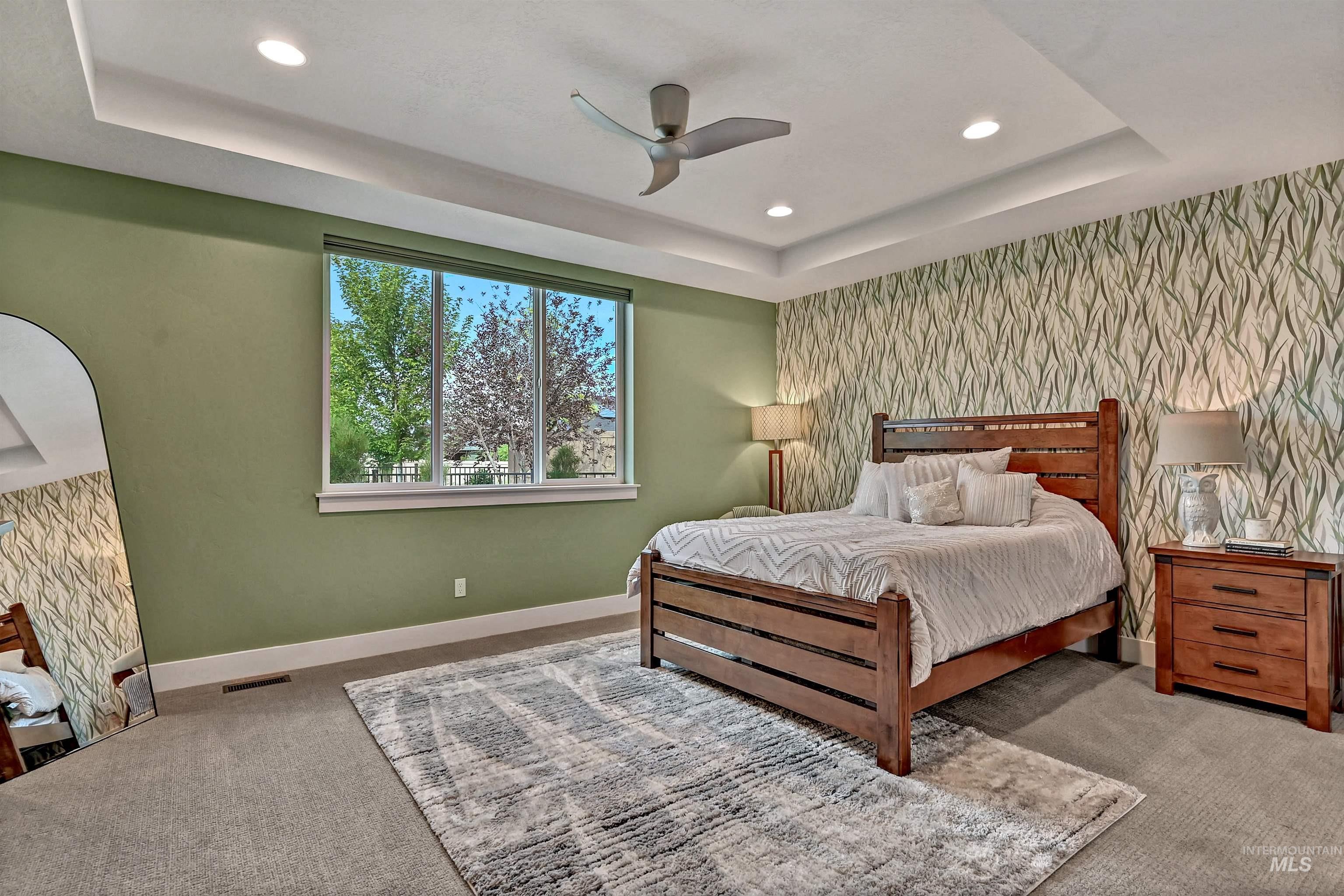 Carpeted bedroom with a raised ceiling, recessed lighting, a ceiling fan, an accent wall, and wallpapered walls