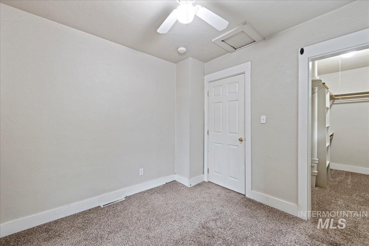 Unfurnished bedroom with a textured wall, attic access, light carpet, a walk in closet, and ceiling fan