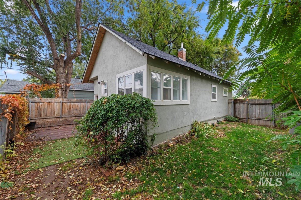 View of side of home with a fenced backyard, stucco siding, a chimney, and roof with shingles