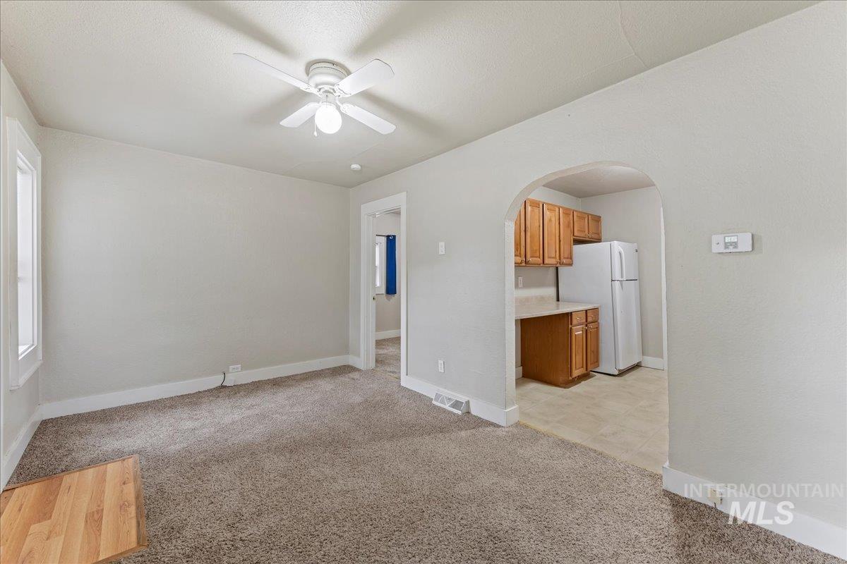 Unfurnished living room featuring light carpet, arched walkways, and ceiling fan