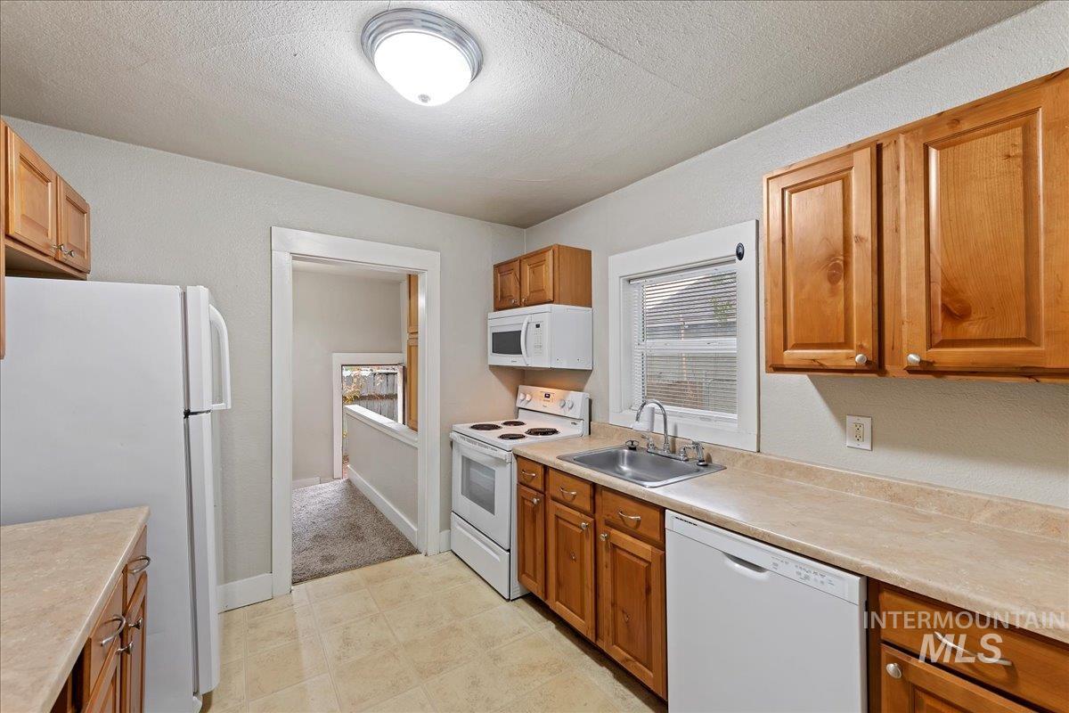 Kitchen with white appliances, light countertops, brown cabinetry, and a textured ceiling
