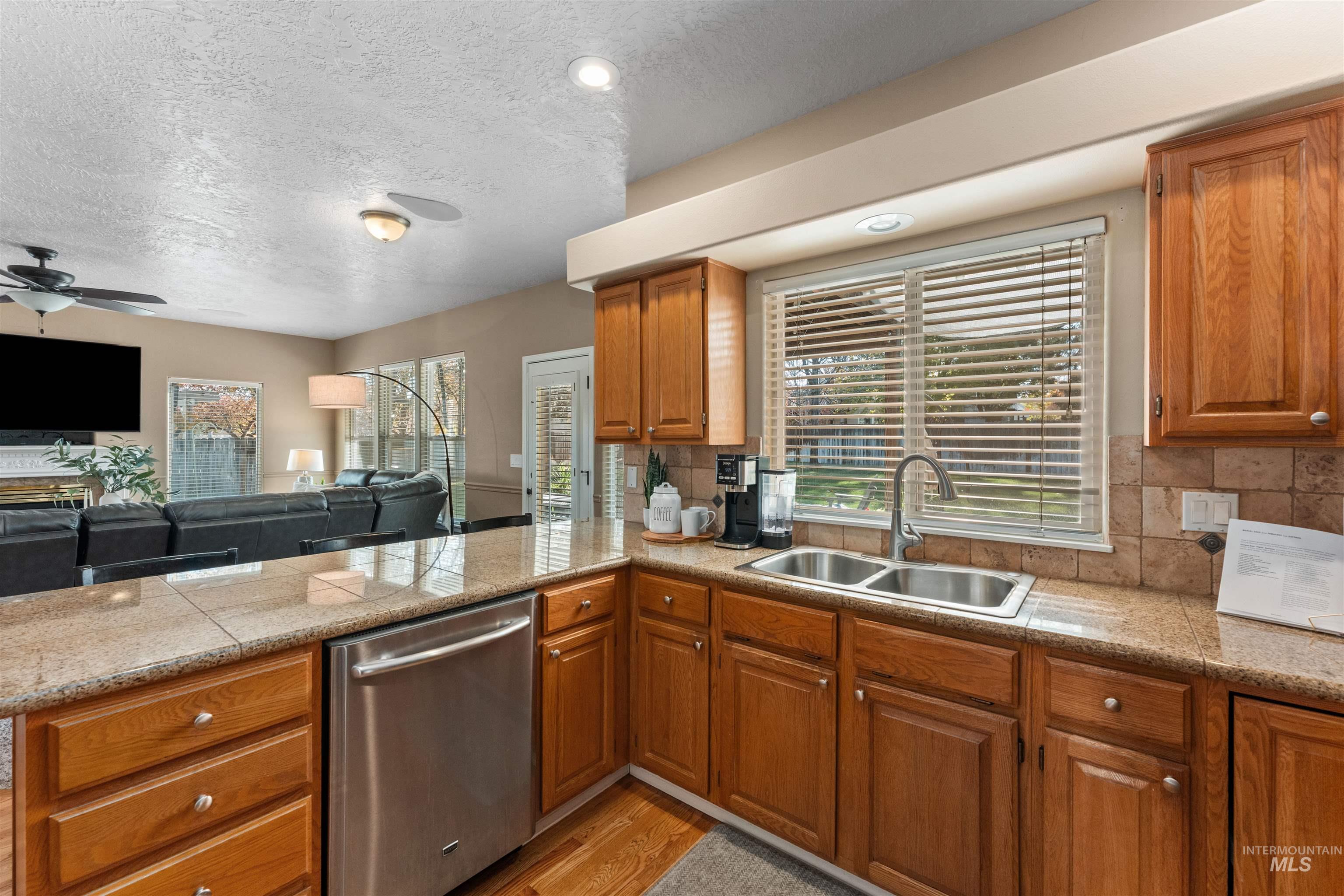 Kitchen featuring open floor plan, stainless steel dishwasher, backsplash, light wood finished floors, and a peninsula