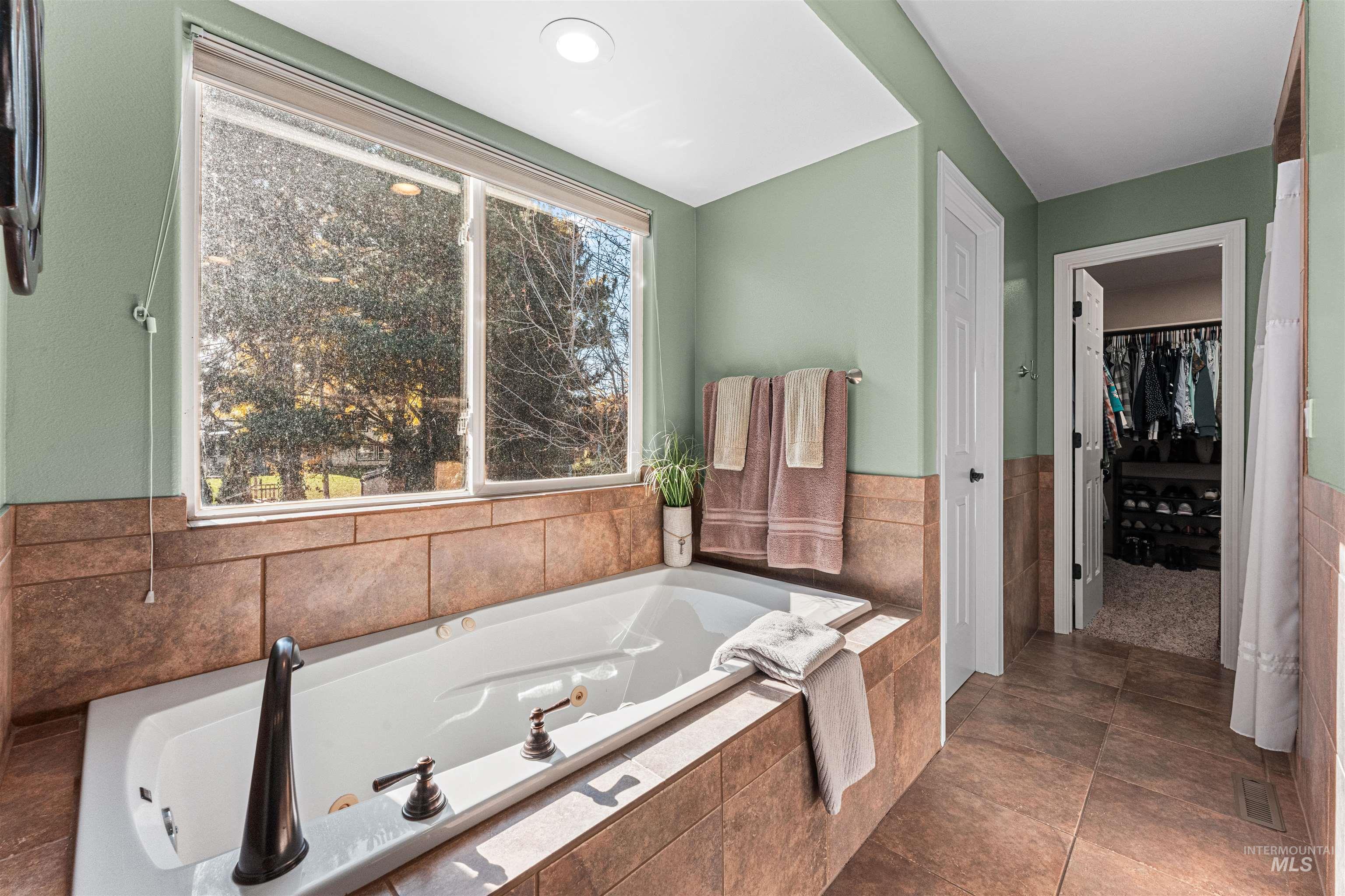 Full bathroom with a tub with jets, a walk in closet, dark tile patterned floors, and recessed lighting